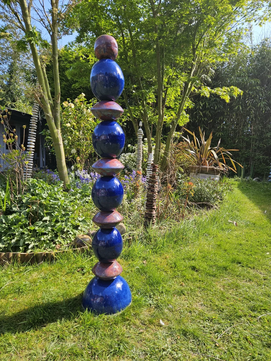 A tall stacked ceramic sculpture in blue and copper glazes standing on a lawn