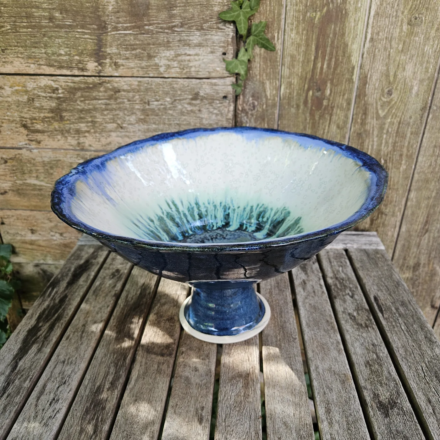A large footed bowl glazed in white, blue and green on a wooden table