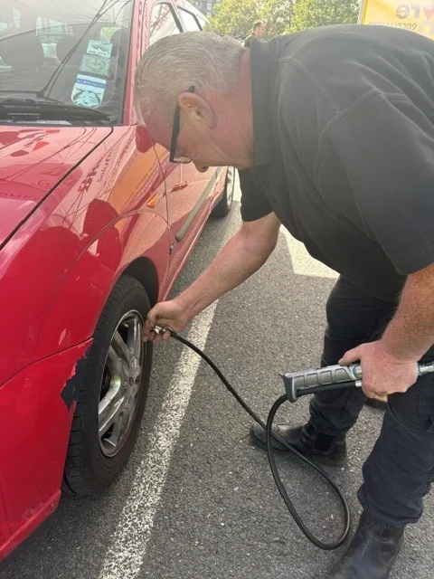 A technician using a hand held gauge on the tyre of a red car