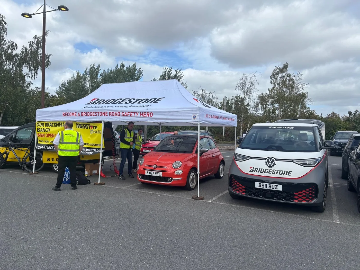 Cars queuing beside the Bridgestone gazebo in a supermarket car park, with staff in high visibility vests working on a red Fiat